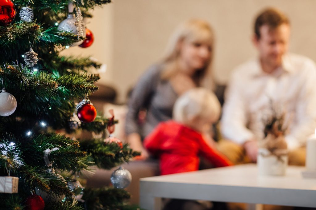 Man, woman and child blurred in background with a Christmas tree in the foreground