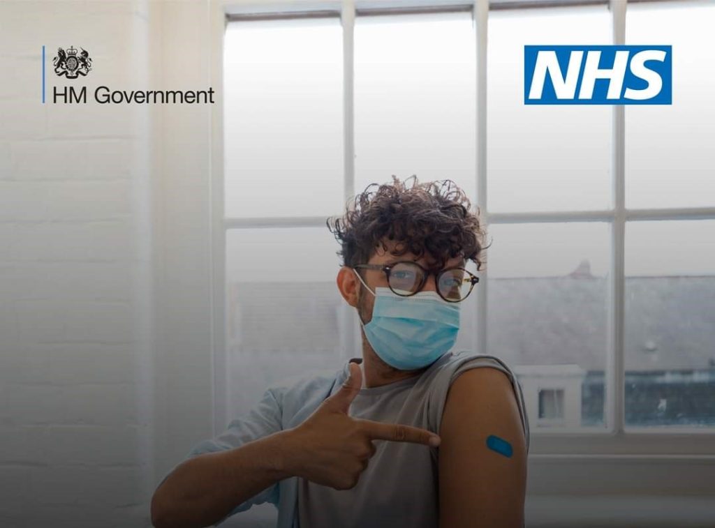 Image of young adult wearing glasses and mask pointing to arm where he's had a covid vaccine