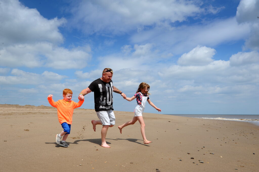 Middle aged man running with young boy and girl on the beach