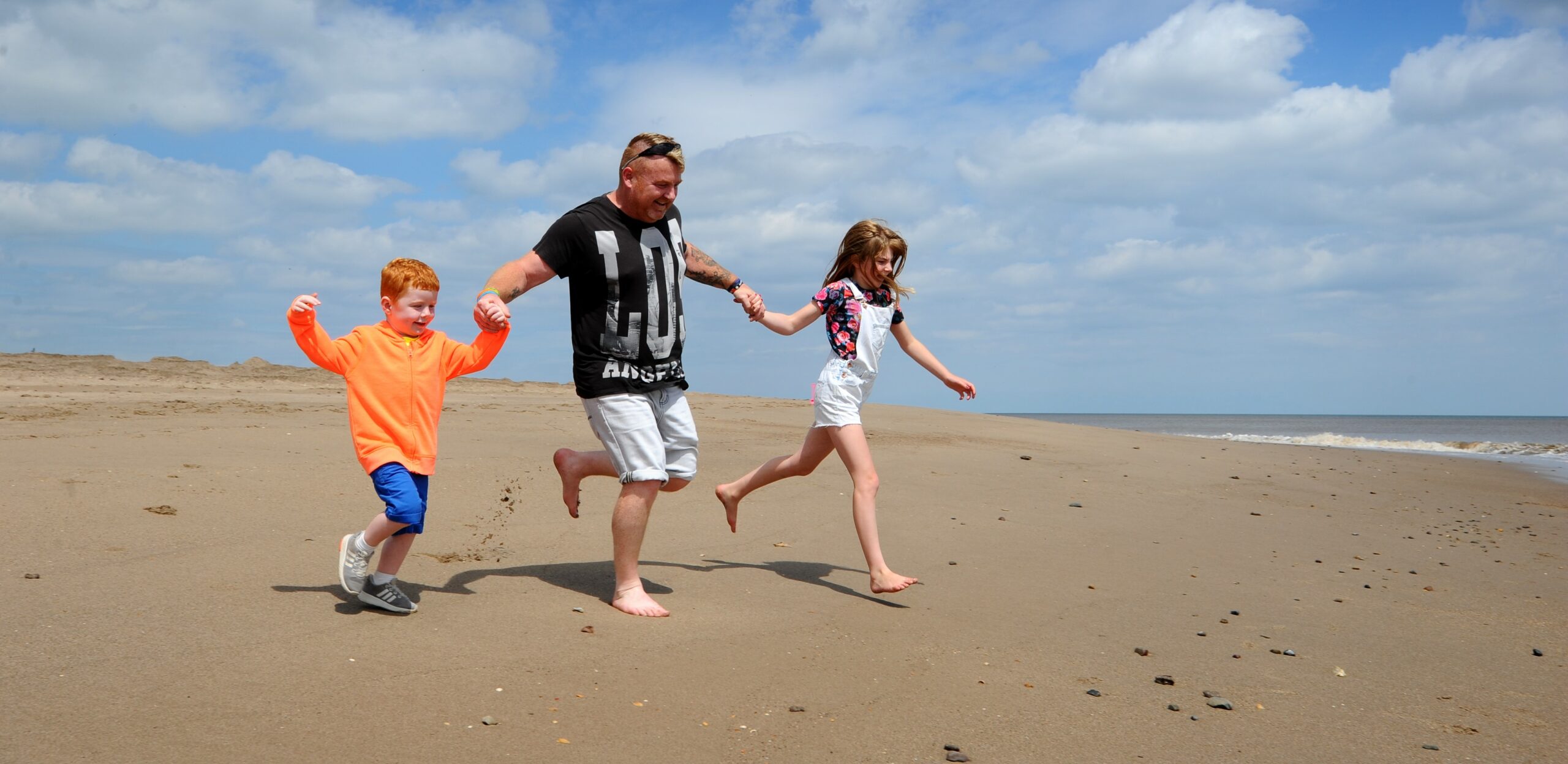 Middle aged man running with young boy and girl on the beach