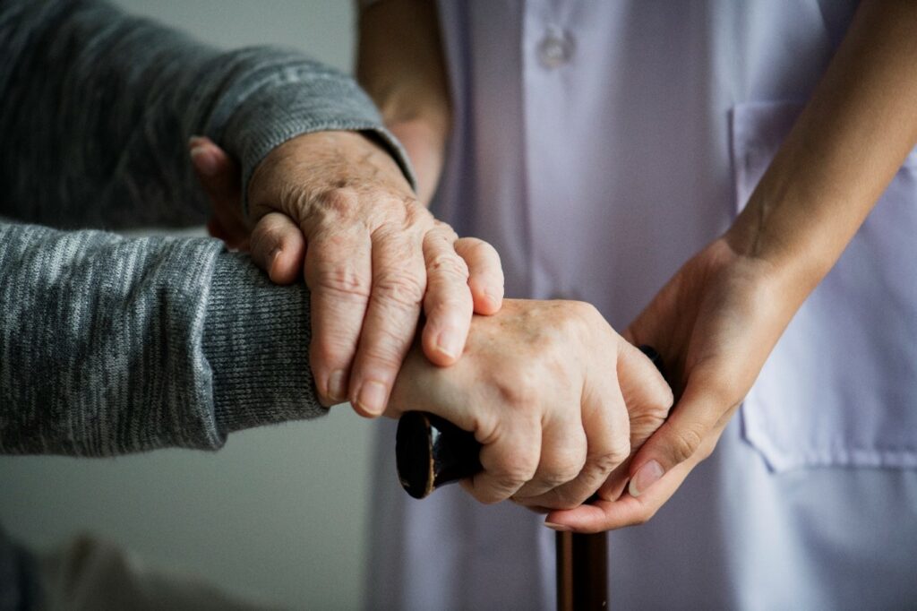Older persons hands resting on the handle of a walking stick, supported by a care worker