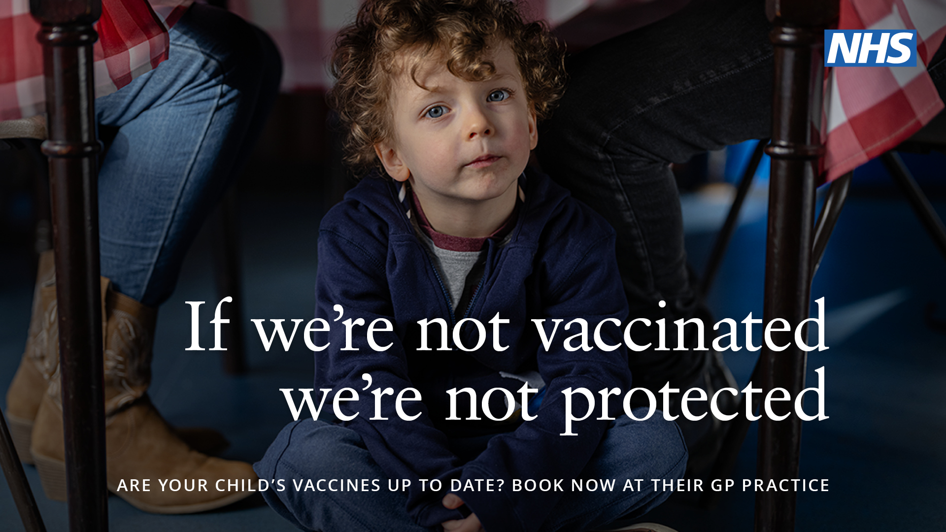 Young boy sat under a table. "If we're not vaccinated we're not protected".