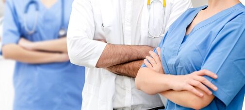 Close-up of diverse medical professionals standing with arms crossed in a bright hospital corridor.