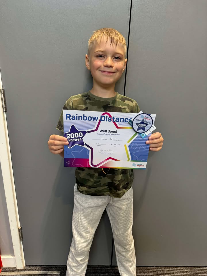 A photo of Jenson holding his Rainbow Distance certificate for completing 2000 metre swim.