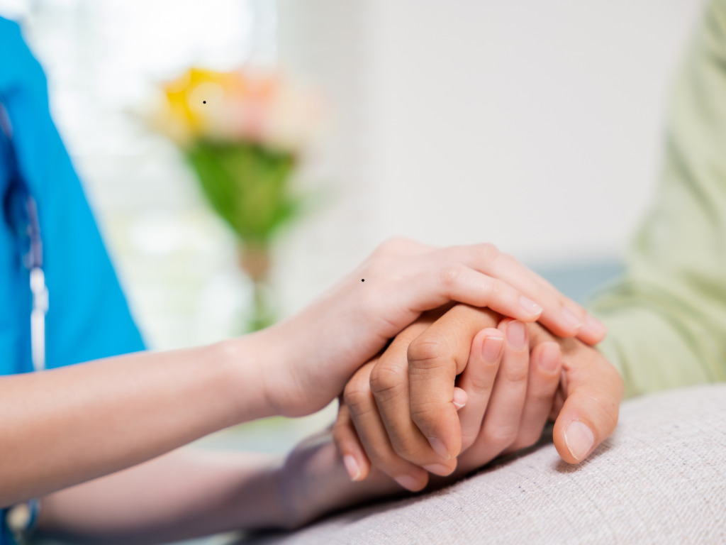 Close-up of a healthcare worker gently holding a patient's hand in a comforting gesture indoors.