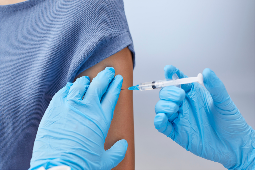 Photograph of a medical professional wearing blue gloves administering a vaccine into someone's arm