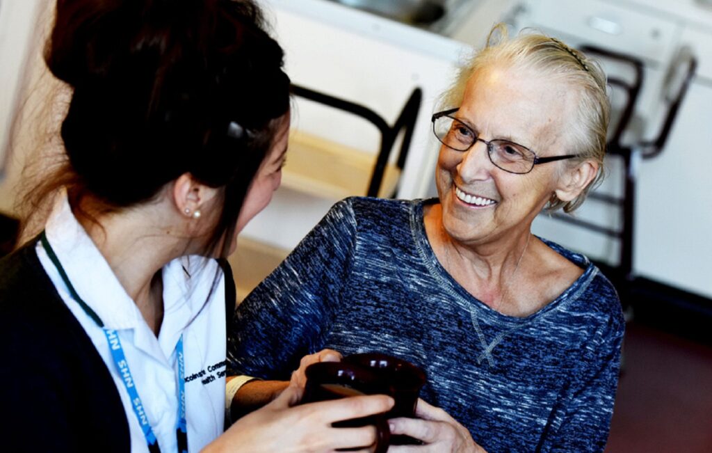 Image of young female health care professional sat speaking with an old woman with glasses