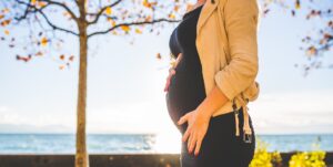 Pregnant woman - focussing on the belly - standing outside public area near the sea in autumn - cropped