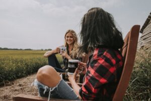 Two female friends sat outside on a bench drinking coffee